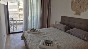 A bedroom with a bed, pillows, a macrame wall hanging, and a view of an outdoor balcony.