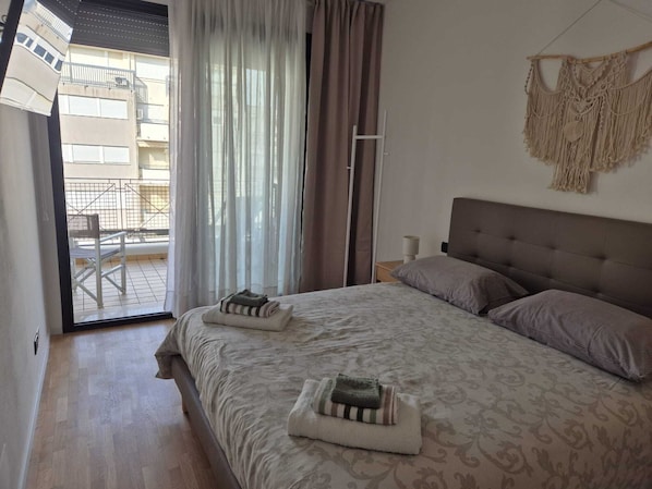 A bedroom with a bed, pillows, a macrame wall hanging, and a view of an outdoor balcony.