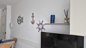 A modern living room with a flat-screen TV, a wooden dining table with chairs, and nautical-themed wall decor.