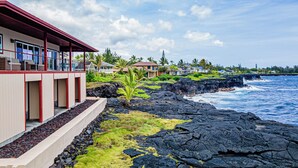 A coastal property with a modern building featuring large windows and a red roof, situated on a rocky shoreline with a view of the ocean. - Paradise Ocean Vista- Absolute Oceanfront gorgeous views, A/C & laundry! (Keaau)