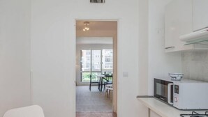 A modern kitchen with white cabinets, a microwave, and a gas stove. There is a dining area with a table and chairs visible through an open doorway. - Charming T4 with parking and terrace - sleeps up to 6 (Avignon)