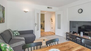 A modern living room with a grey sofa, a wooden dining table, and a TV. - Charming T4 with parking and terrace - sleeps up to 6 (Avignon)