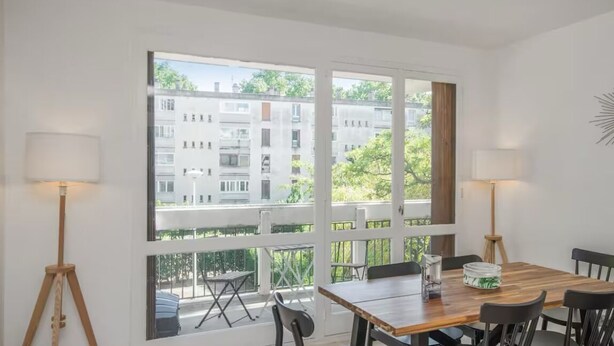 A room with a wooden table and chairs, large windows, and a view of buildings and greenery outside. - Charming T4 with parking and terrace - sleeps up to 6 (Avignon)