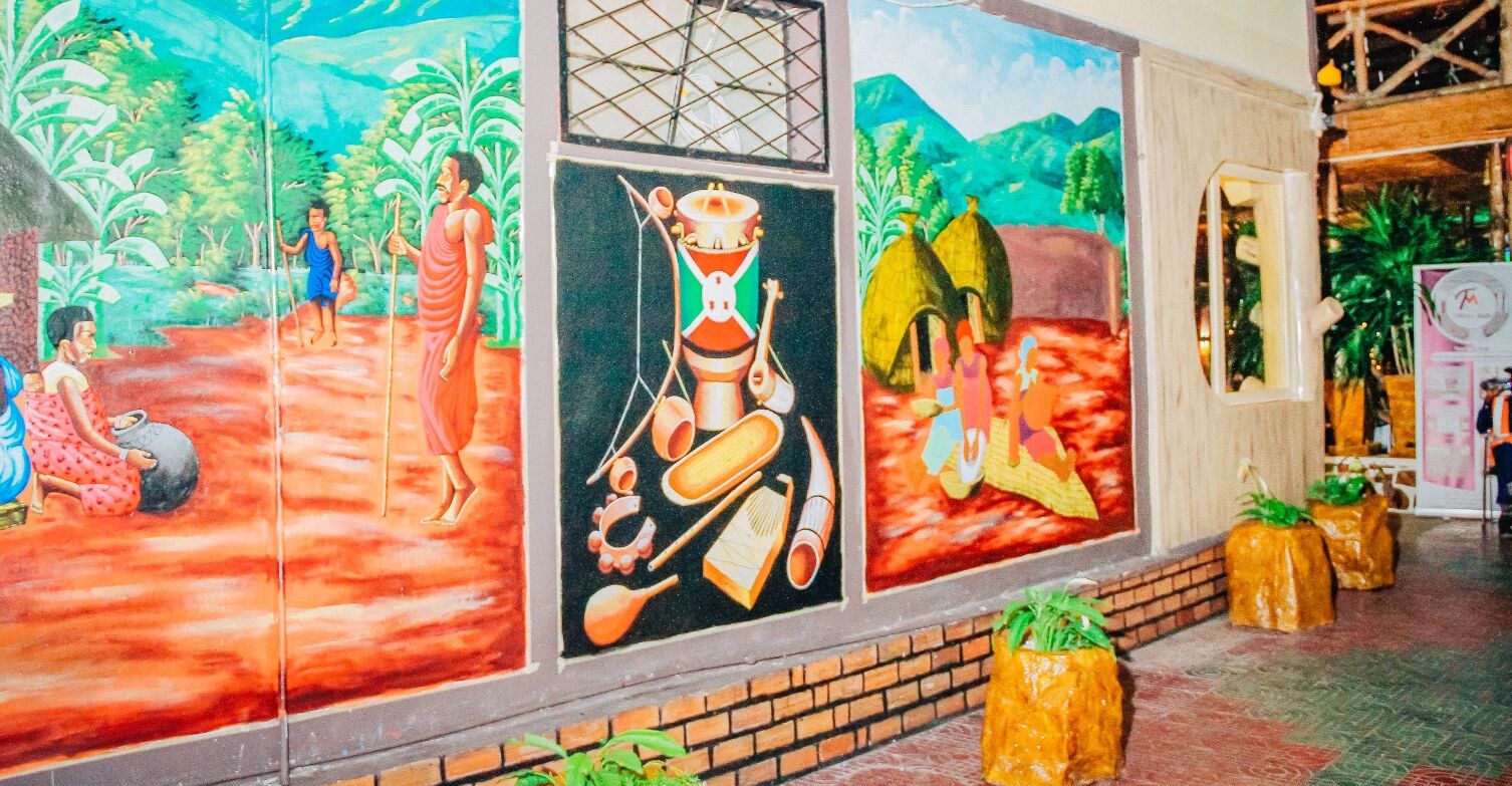 A mural with cultural scenes and a brick wall.