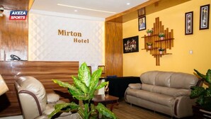 A lobby with a reception desk, a leather sofa, and a wooden reception desk. - Mirton Hotel (Bujumbura)