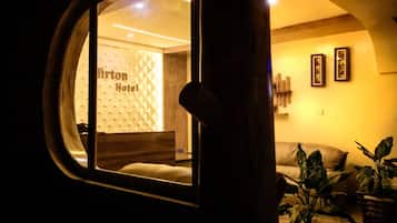 A view through a window of a hotel room with a visible bed, a wooden headboard, and a wall with framed pictures.