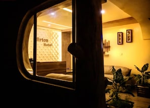 A view through a window of a hotel room with a visible bed, a wooden headboard, and a wall with framed pictures. - Mirton Hotel (Bujumbura)