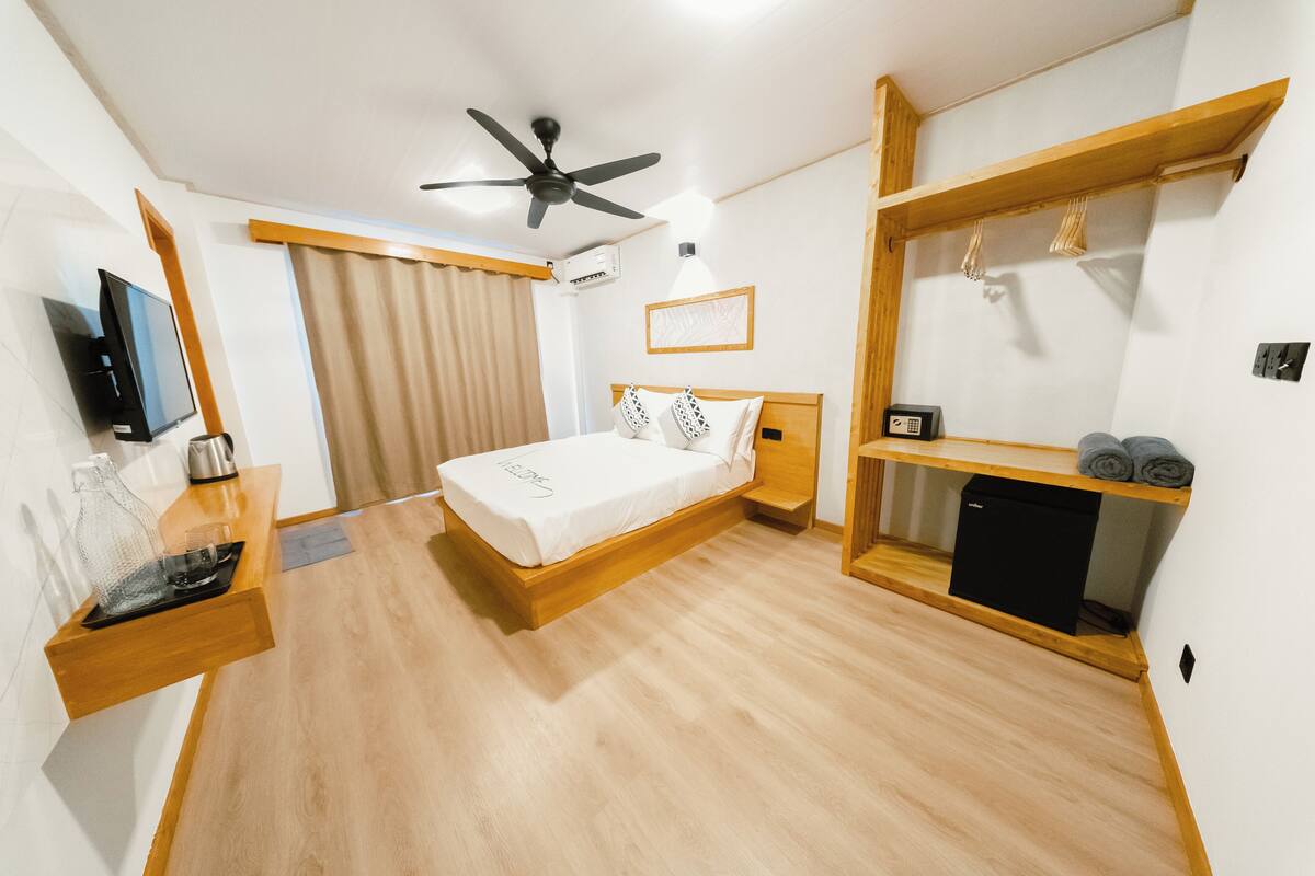 A modern hotel room with a wooden bed, a flat-screen TV, a ceiling fan, and a built-in shelf with towels.