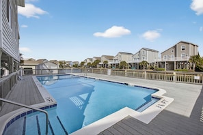 A swimming pool with a wooden deck, surrounded by residential buildings. - Cozy 3-bedroom condo in charming Ocean Isle Beach with 5 minute walk to beach (Ocean Isle Beach)