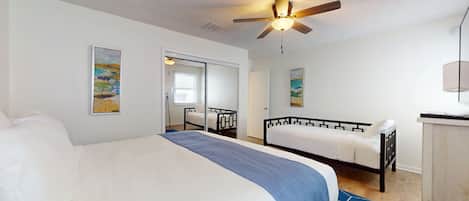 A bedroom with a large bed, a smaller bed, a ceiling fan, and artwork on the walls.