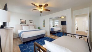 A hotel room with a bed, a desk, a ceiling fan, a TV, and a large mirror.