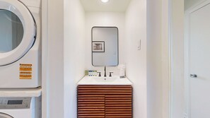 A bathroom with a washing machine, a sink with toiletries, and a mirror.