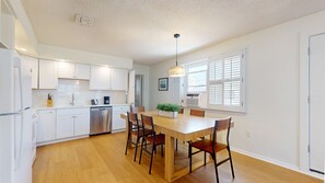 A modern kitchen with white cabinets, a stainless steel dishwasher, and a wooden dining table with chairs.
