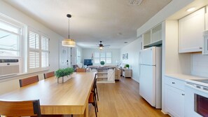 A modern kitchen with a wooden dining table, white cabinetry, and a ceiling fan.