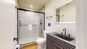 A modern bathroom with a glass-enclosed shower, a white toilet, and a sink with a mirror above.