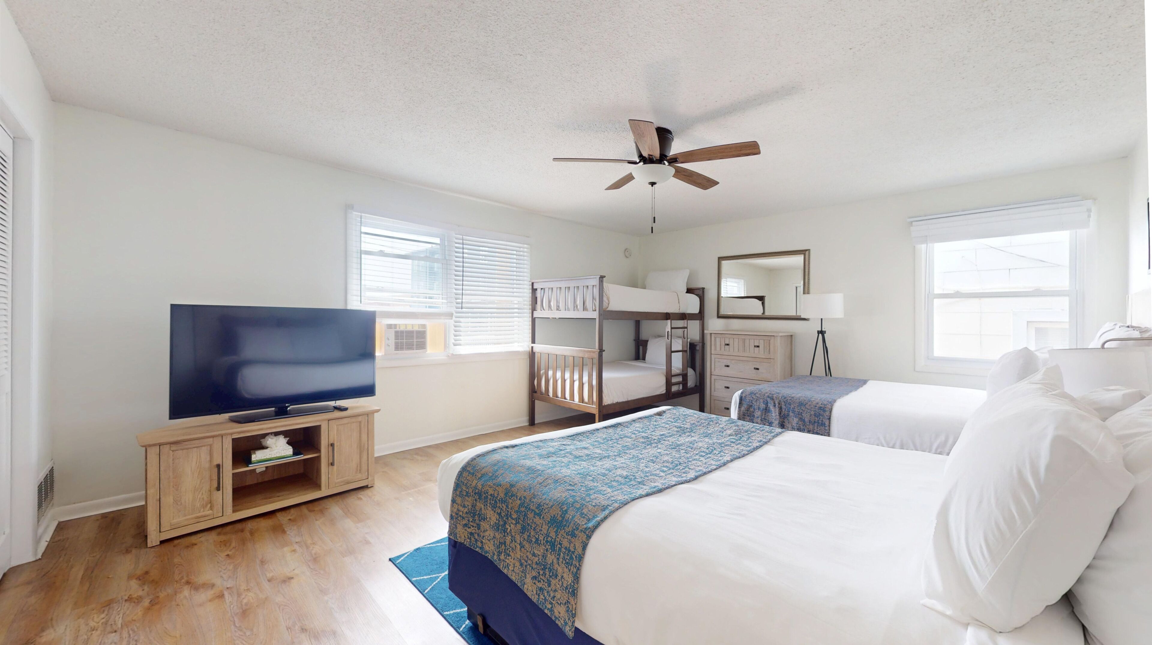A bedroom with a TV, bunk beds, a ceiling fan, a dresser, and a mirror.