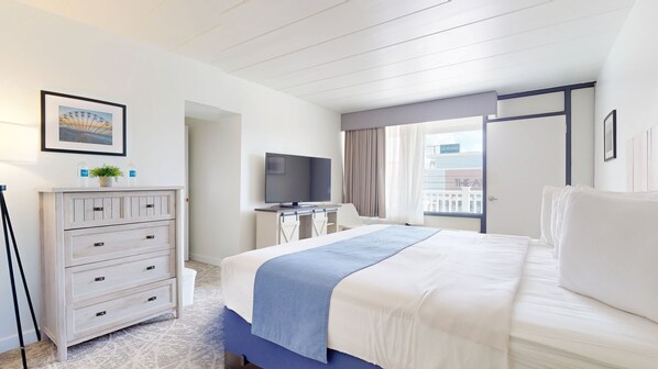 A hotel room with a bed, a TV, a dresser, and a window with a view of the ocean.