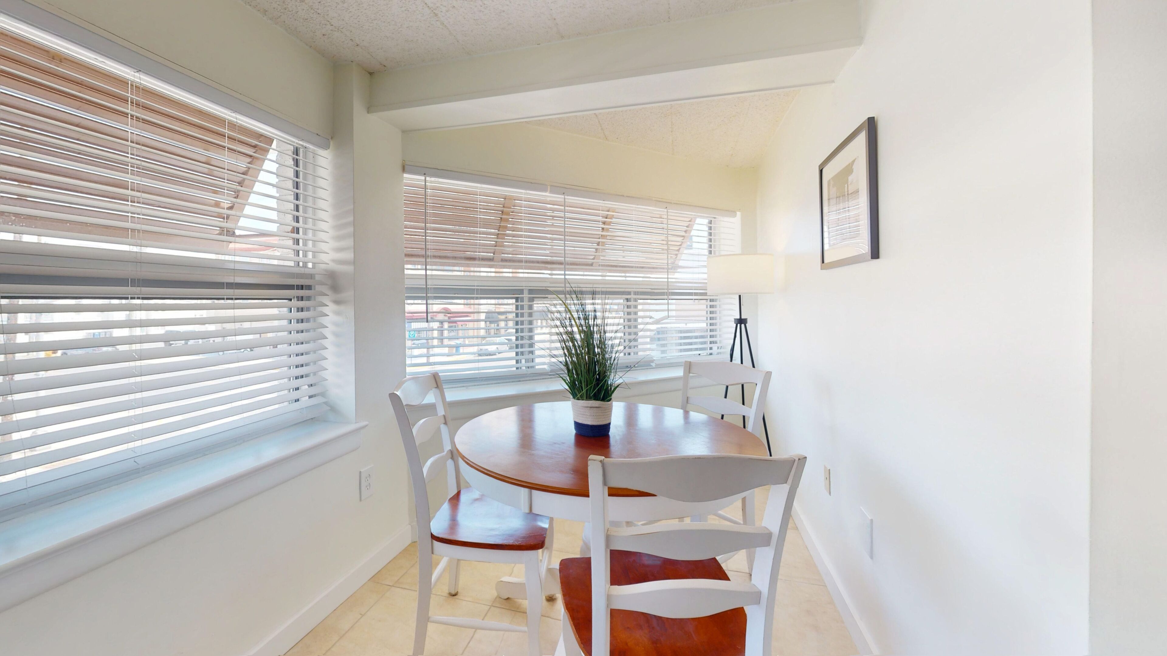 A dining area with a round table, white chairs, and a potted plant.