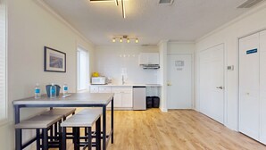 Uma cozinha moderna com armários brancos, micro-ondas e cafeteira. Há uma mesa de jantar com bancos e um quadro na parede.
