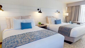 A hotel room with two beds, a bedside table with a clock, a lamp, and a view of the outside through a window. - Balcony Queen Suites (Ocean City)