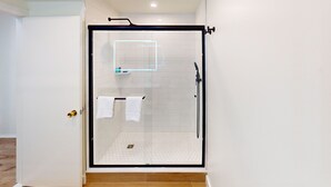 A glass-enclosed shower with a white tiled floor and a black frame. - Queen Suite Upper (502) (Ocean City)