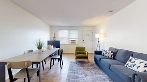 A modern living room with a dining area, a sofa, a lamp, and a chair.