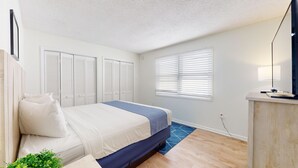 A bedroom with a bed, a desk, and a window with blinds.