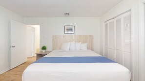 A bedroom with a bed, a nightstand, a potted plant, and a closet.
