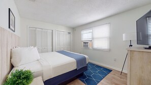 A hotel room with a bed, a desk with a TV, a window with blinds, and a notice on the door.