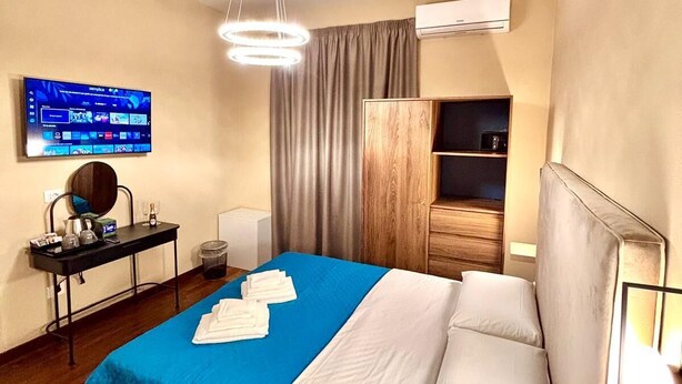 Ein Hotelzimmer mit einem großen Bett, einem flachbildfernseher an der Wand, einem Schreibtisch mit Stuhl und einem Kleiderschrank.