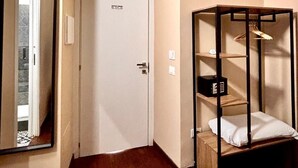 Ein Hotelzimmer mit einer weißen Tür, einer Klimaanlage darüber, einem Holzboden und einem kleinen Holzkästen mit einem weißen Kissen.