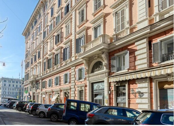 Fila de automóviles estacionados a lo largo de una calle con un edificio de varios pisos de arquitectura clásica.