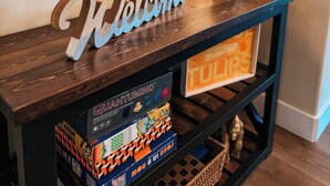 Una consola de madera con un cartel que dice 'Welcome', una lámpara y un estante con juegos de mesa.