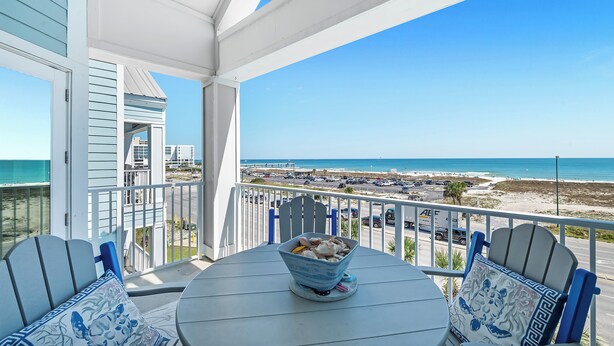 A balcony with a table and chairs, a bowl of food, and a view of the beach and ocean.