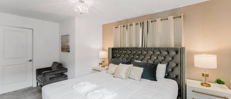 Un dormitorio ordenado con una cama grande, dos mesitas de noche, una silla y una puerta.