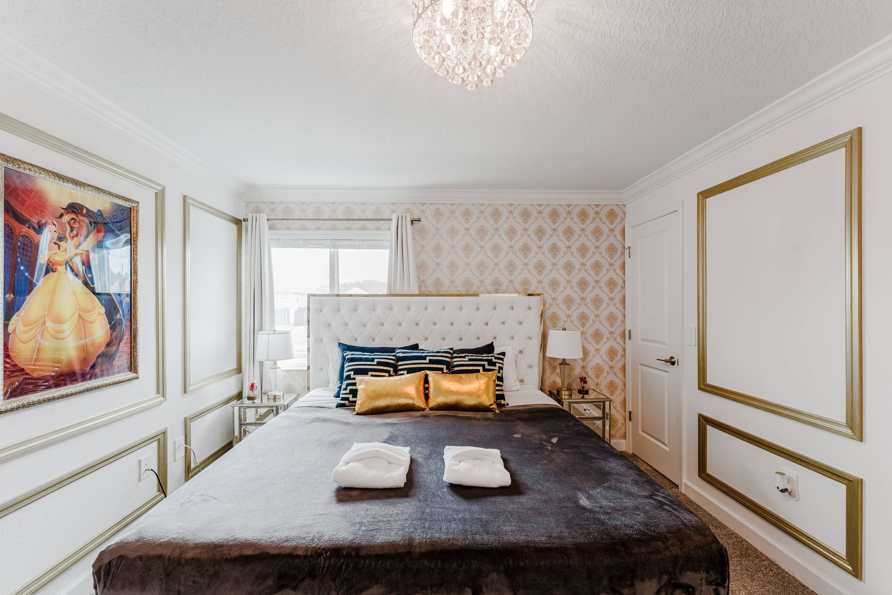 Hotellihuone, jossa on suuri sänky, kattokruunu ja taulu seinällä.