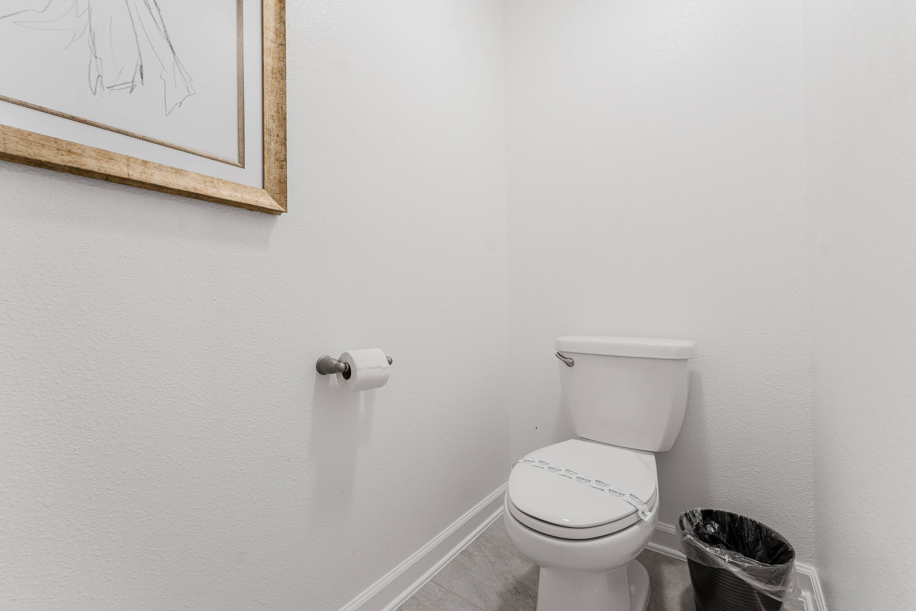 A bathroom with a toilet, a roll of toilet paper, and a trash can.