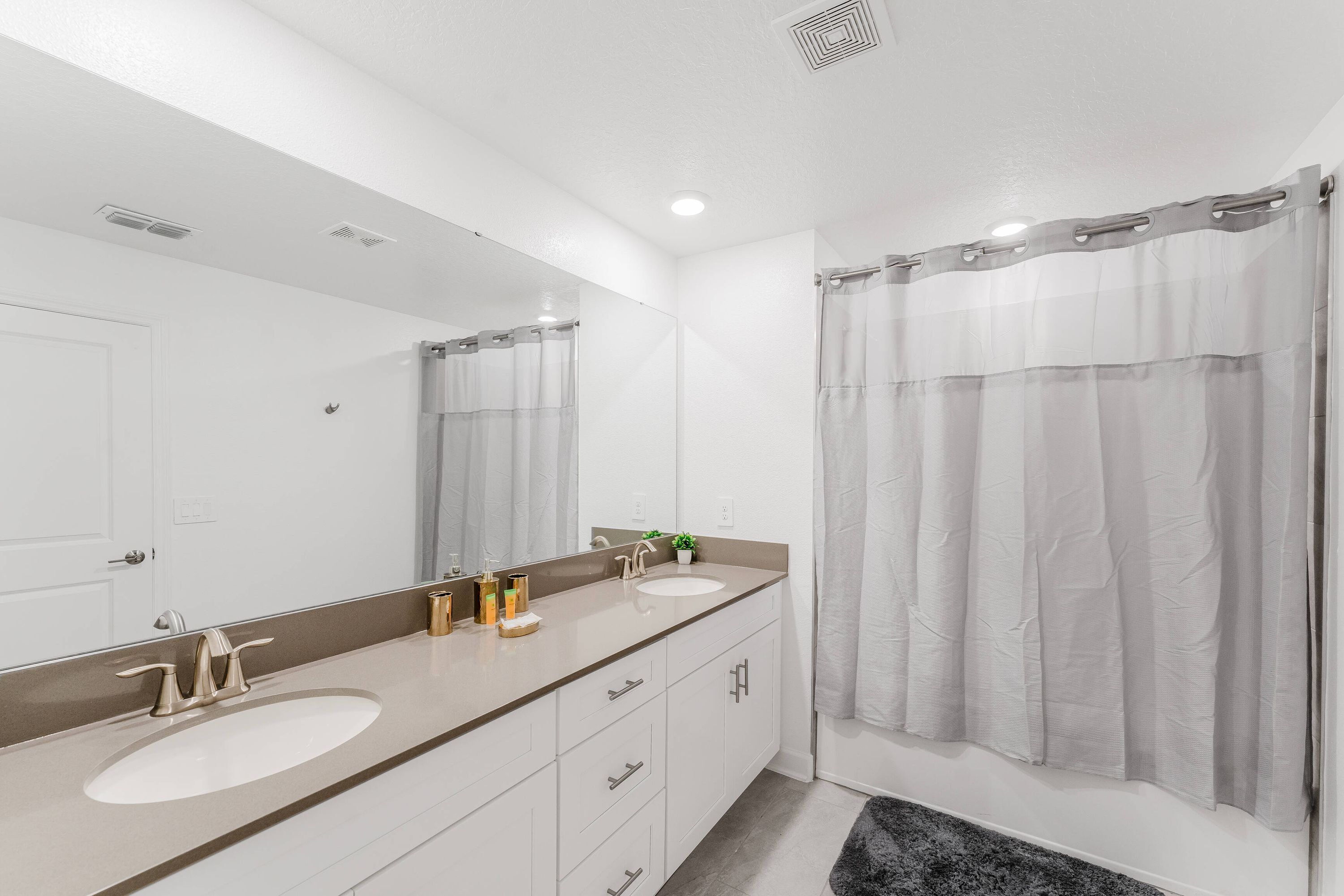 Une salle de bain moderne avec deux lavabos, un grand miroir et un rideau de douche.