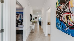 A hallway with a bed, a table with a vase, and a large abstract painting on the wall.