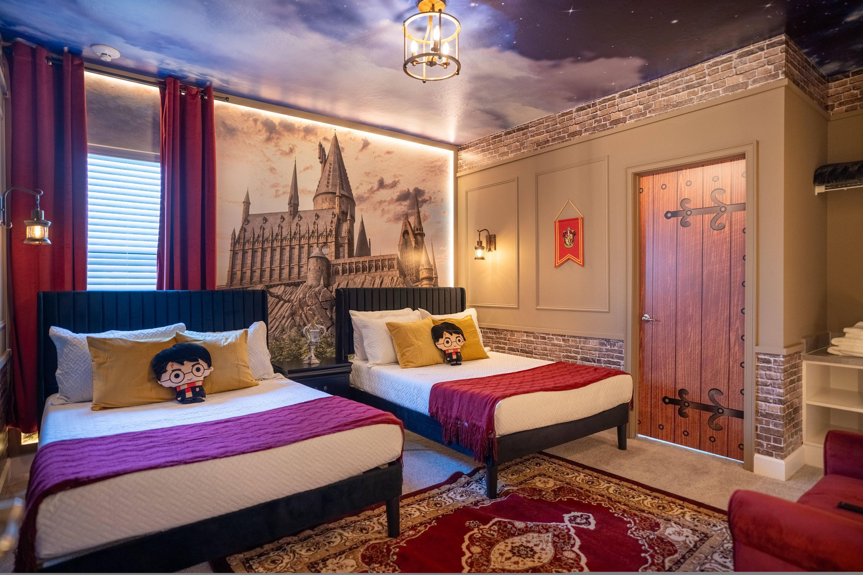 A bedroom with two beds, a mural of a castle, a red door, and a chandelier.