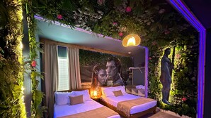 A room with two beds, a large mirror, and a wall with artificial greenery and flowers.