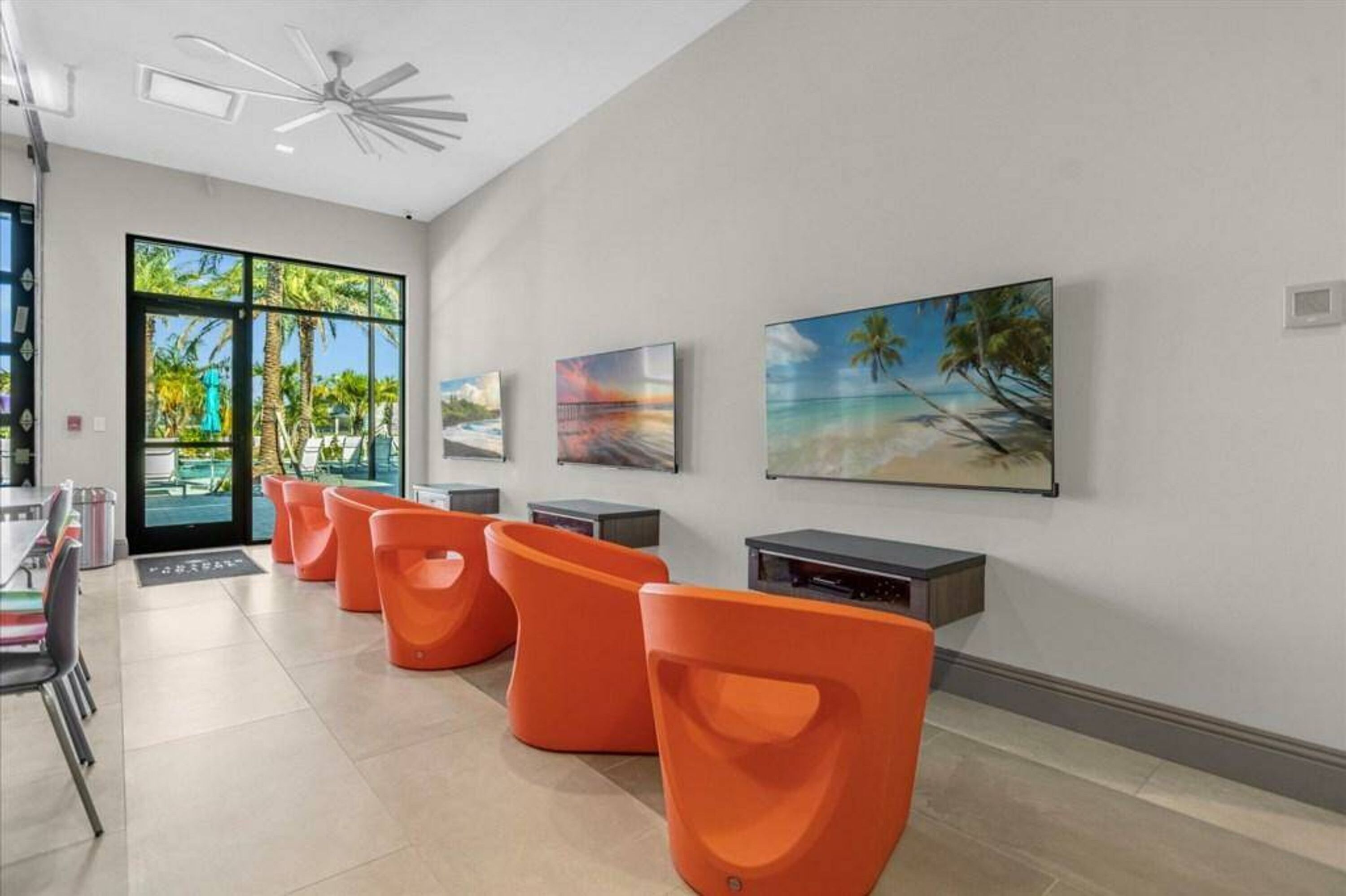 A modern interior with orange seating, a ceiling fan, and tropical-themed artwork on the walls.