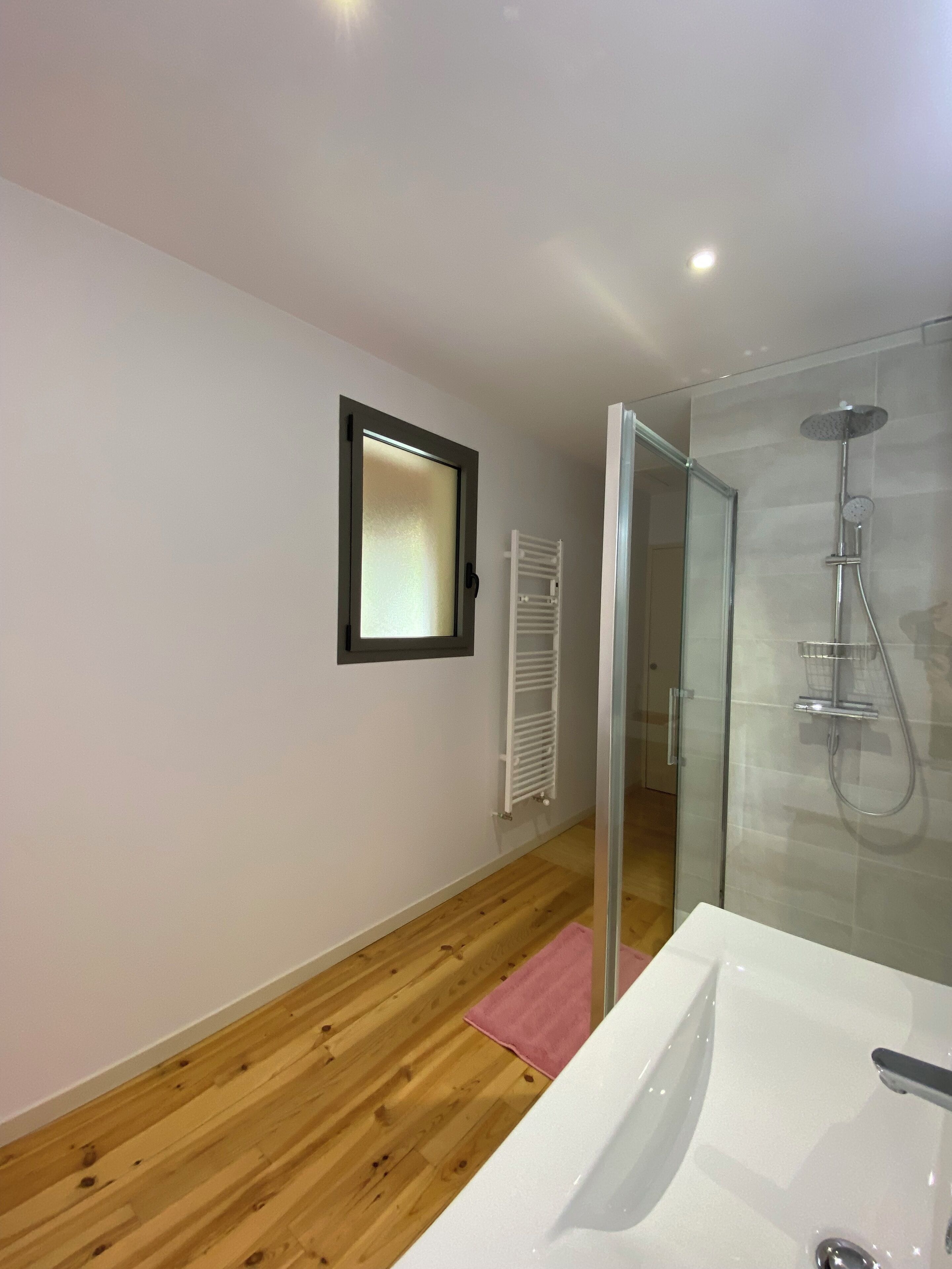 Un baño moderno con cabina de ducha de vidrio, un lavamanos blanco y suelo de madera.