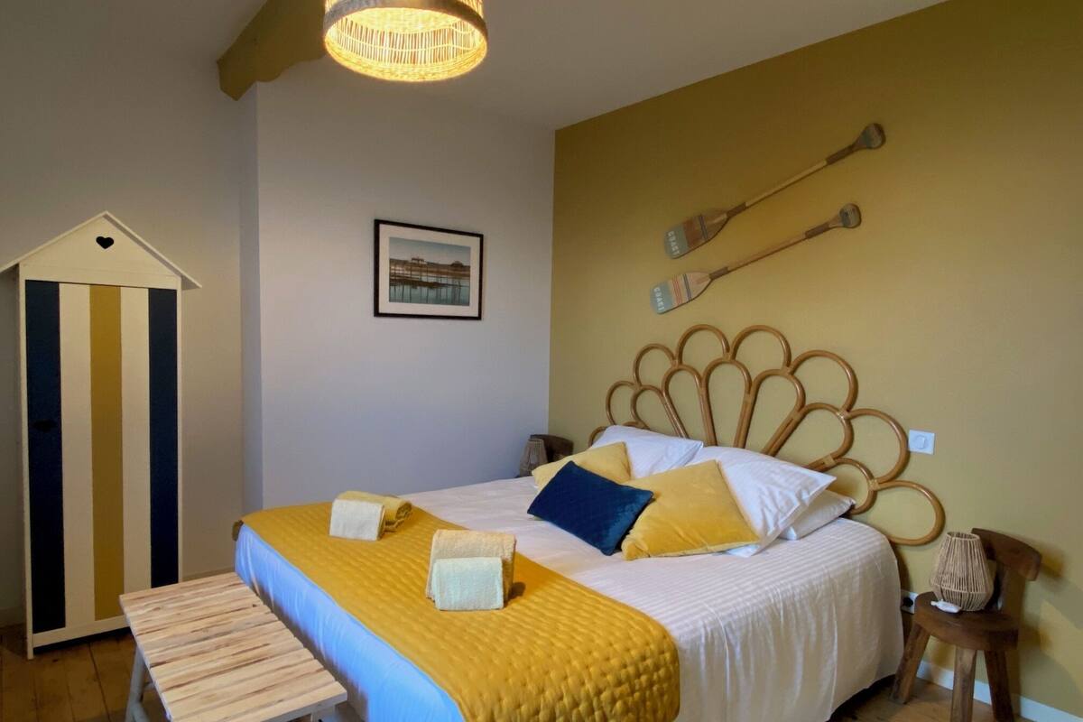 Ein Schlafzimmer mit einem Bett, einer Holzbank, einer Hängeleuchte und einem Wandbild.