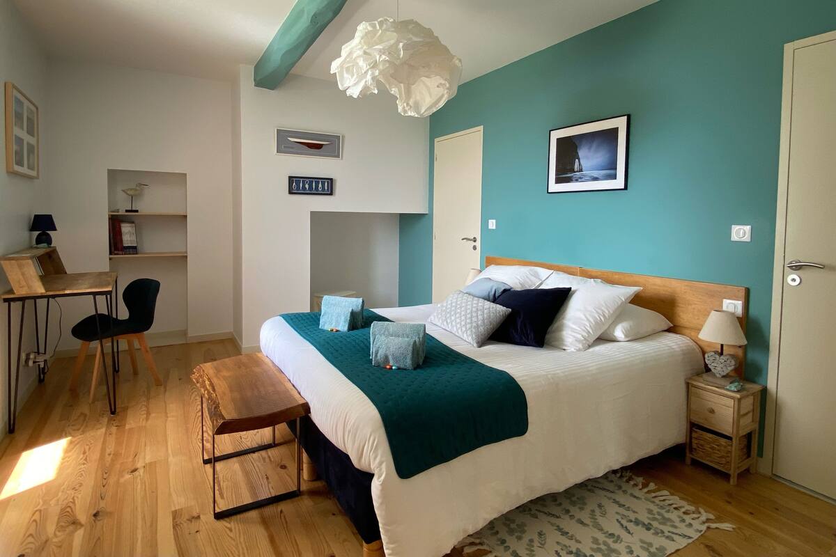 Ein Schlafzimmer mit Bett, Nachttisch, Sessel, Schreibtisch und Regalen.