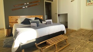Ein Schlafzimmer mit einem Holz-Kopfteil, einem Bett mit weißer und grauer Bettdecke, mehreren Kissen, einer Holzbank und Ski an der Wand.