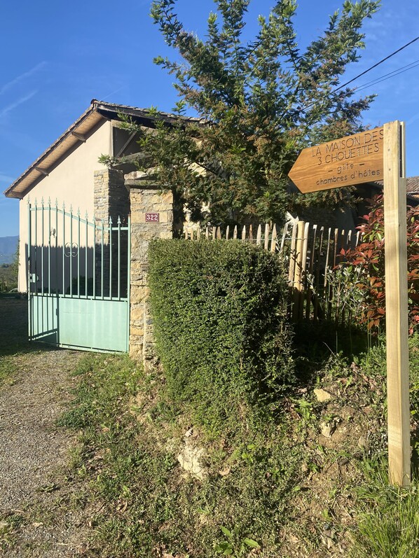 Um edifício rústico com fachada de pedra, portão de metal e placa de madeira indicando ser uma pensão com 3 quartos.