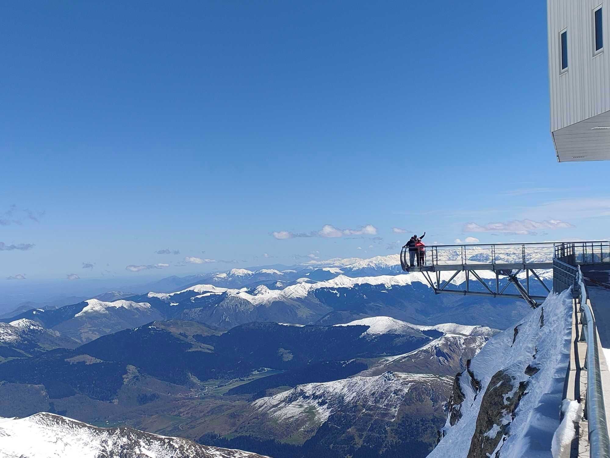 Een panoramisch uitzicht op een bergachtig landschap met een besneeuwde bergtop op de voorgrond en een helderblauwe lucht.