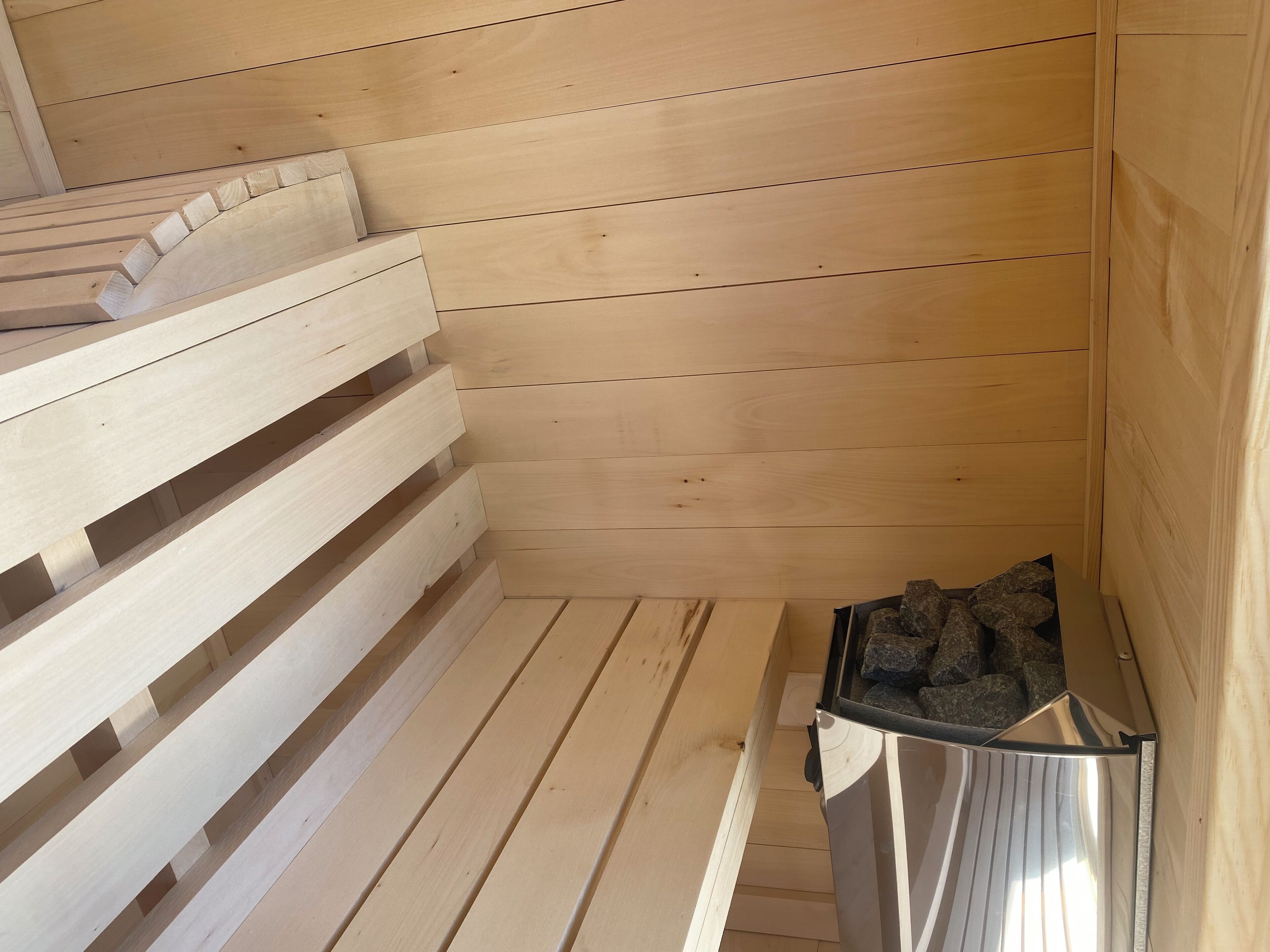 A sauna room with wooden benches and a metal container with stones.