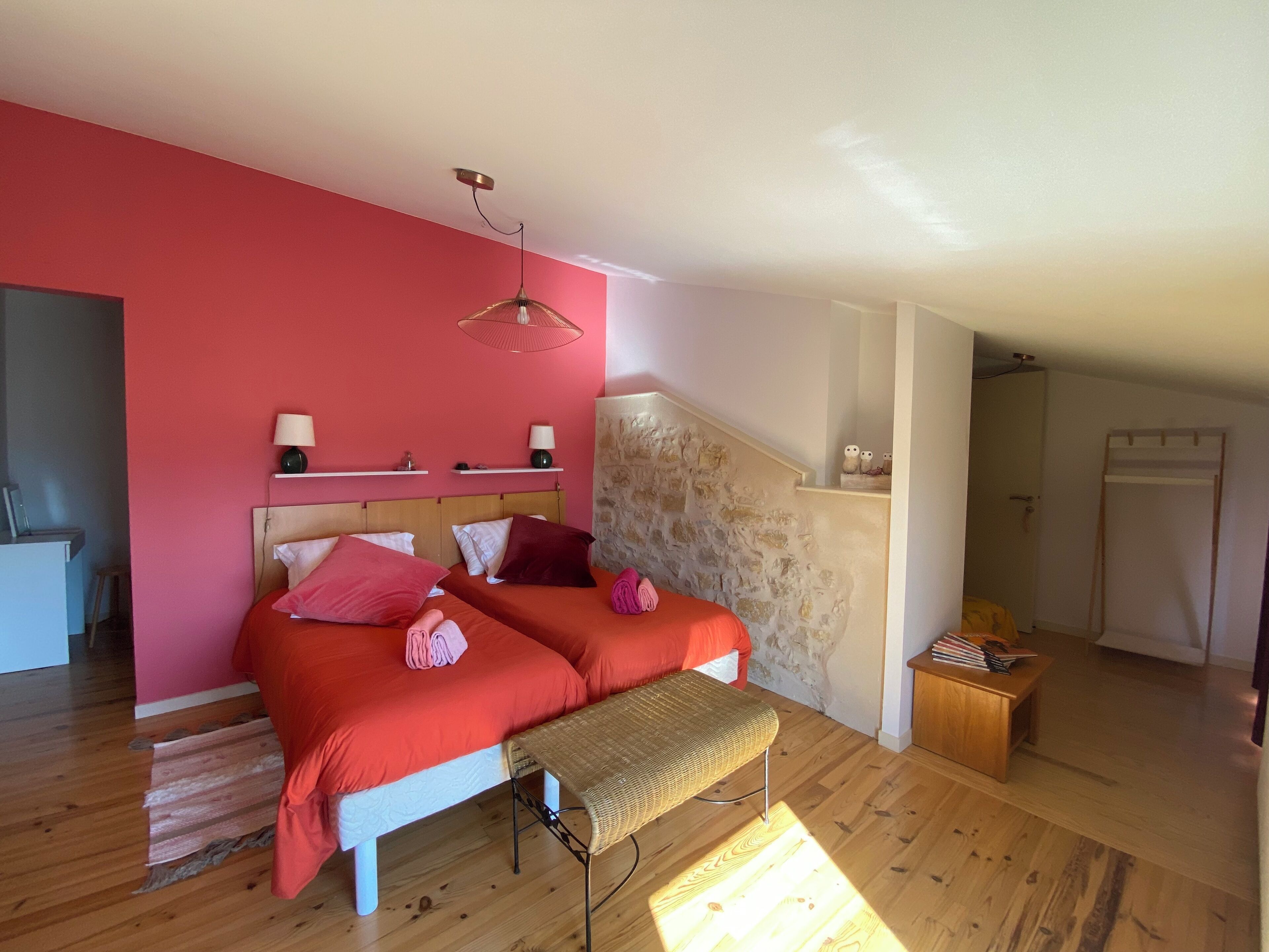 Un dormitorio con dos camas, una pared de piedra, un banco de madera y una mesita con libros.